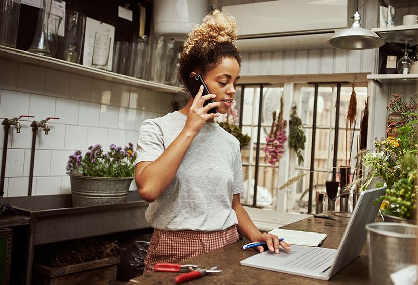 woman in kitchen talking on phone and working on laptop